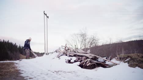 Mann,-Der-Alte-Gebrauchte-Holzbretter-Aus-Einem-Verschneiten-Lager-Aufsammelt,-Um-Sie-Im-Winter-Wiederzuverwenden