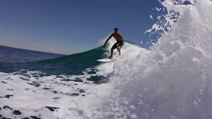 Dynamic video shot capturing a surfer riding a massive wave from a low-angle perspective