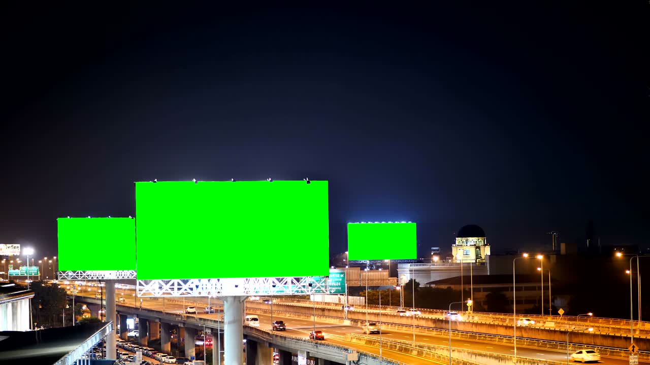 Grøn skærm på reklameskilt på motorvej i skumringen med bybaggrund i Bangkok, Thailand.