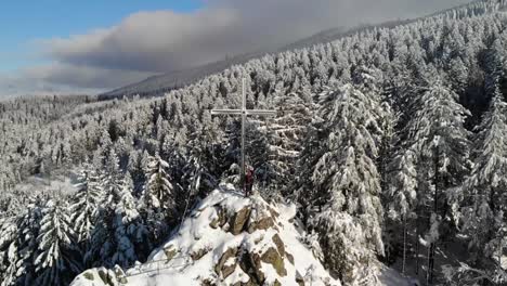 a couple stands next to a summit cross surrounded by a snowy winter landscape in the black forest