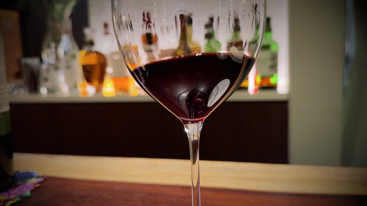 Primo piano di vino rosso che vortica all'interno di un calice di cristallo su un bancone di bar fiocamente illuminato.