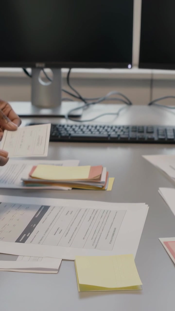 Vertical video: Pointing to form, clerk hand reading and placing ID for filing at desk near screens