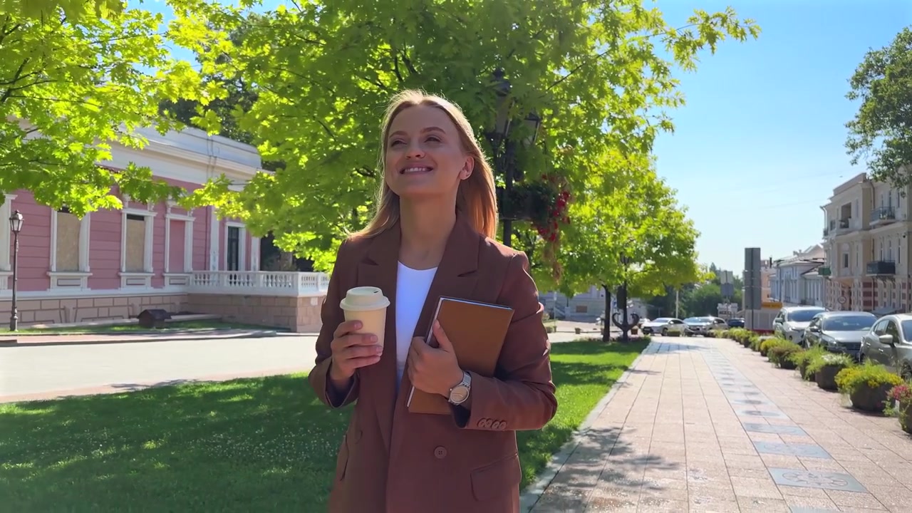 Giovane donna professionista che cammina all'aperto con caffè e taccuino.