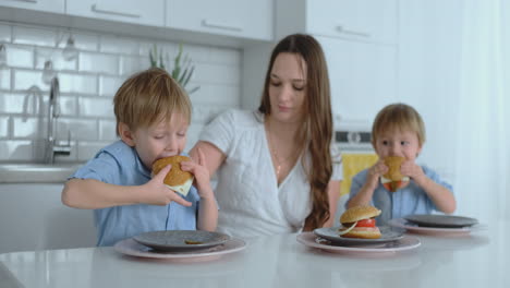 Two-kids-in-blue-shirts-eating-burgers-in-the-bright-kitchen