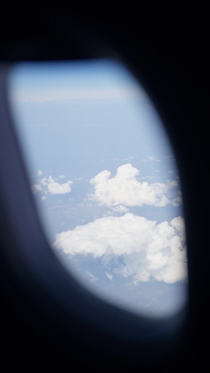 Aerial view of white, fluffy clouds above fields seen from an airplane window. Vertical
