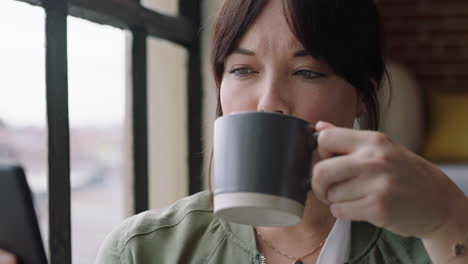 hermosa mujer joven usando un teléfono inteligente bebiendo café en casa disfrutando de una mañana relajada navegando por los mensajes de las redes sociales mirando por la ventana enviando mensajes de texto en el teléfono móvil