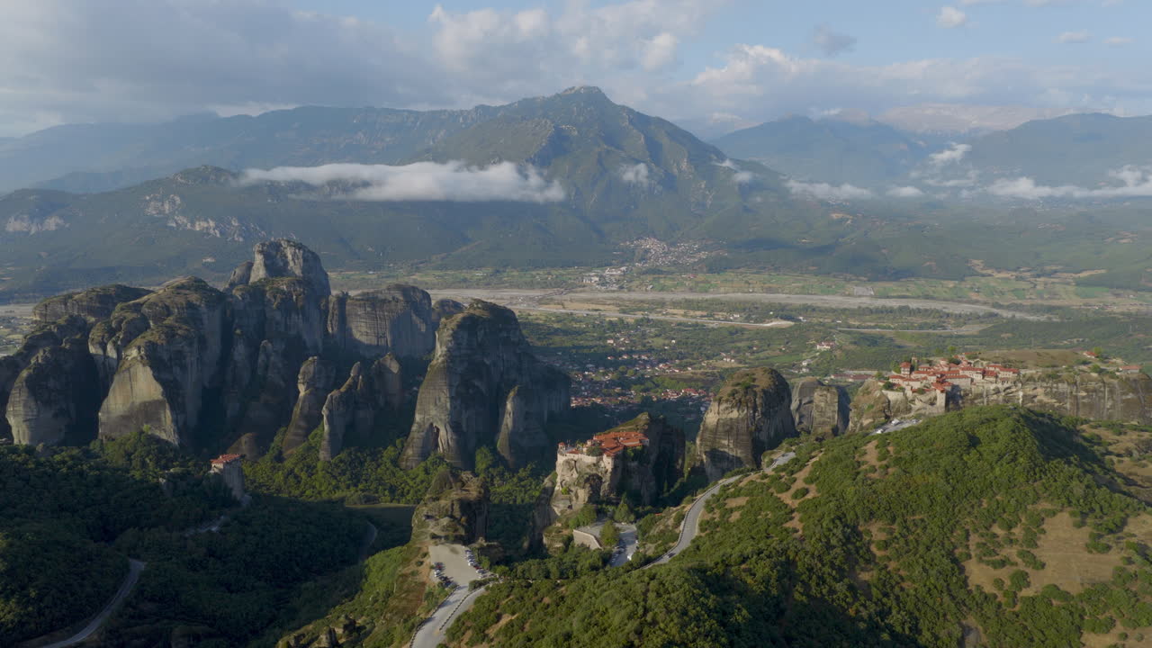 Cinematic aerial view of Meteora monastery in Greece perched on towering cliffs, dramatic rock formations and lush green valley create a breathtaking historic scene