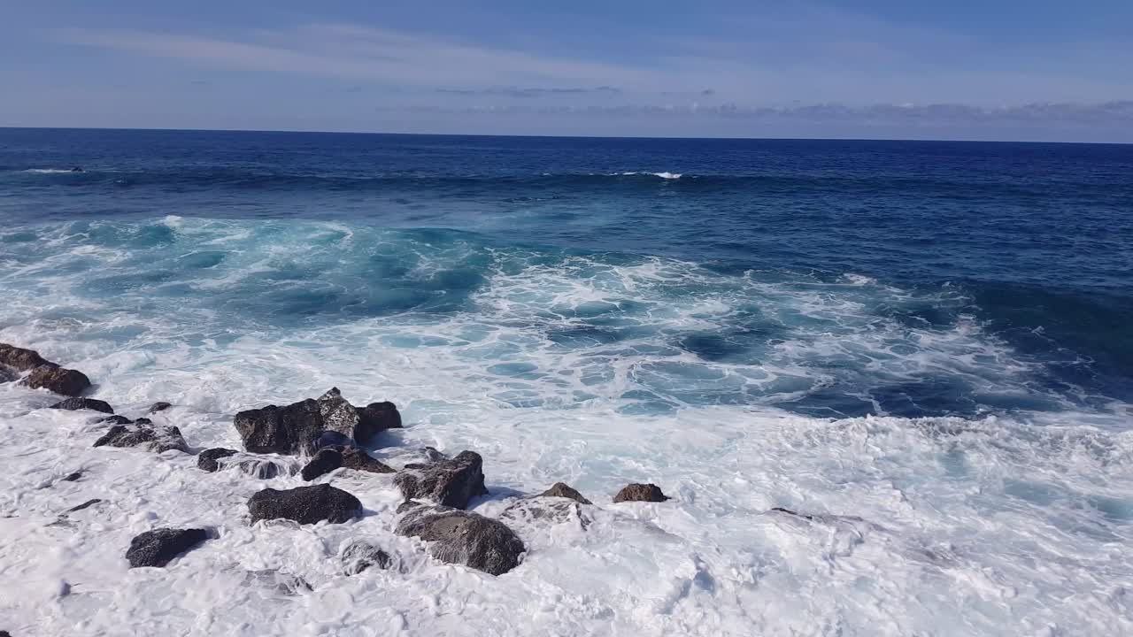 The beautiful blue waves crashing on the rocky shores of the Canarian Islands, Spain - wide shot