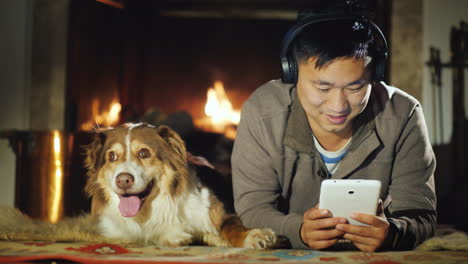 Asian-Man-Uses-A-Tablet-Lies-Near-The-Fireplace