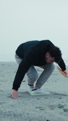 sad man starts reading a book sitting on the sand in winter