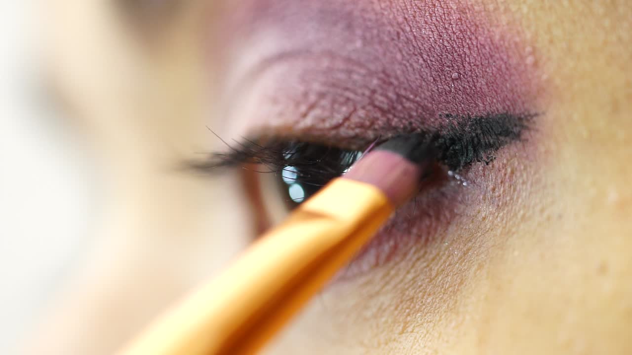 Close-up of a woman applying purple and pink eyeshadow with a makeup brush