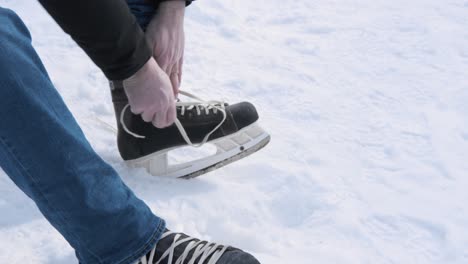 Varón-Caucásico-Atar-Patines-De-Hielo-En-Una-Pista-De-Patinaje-Al-Aire-Libre