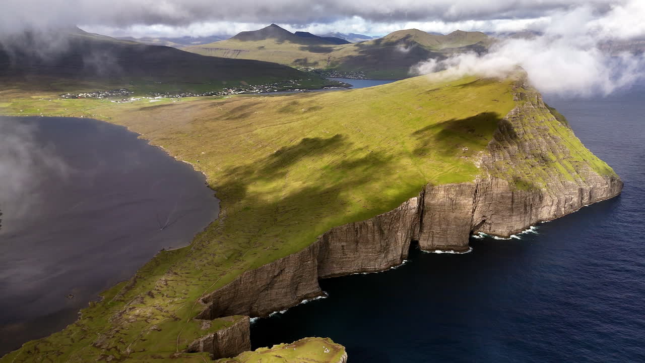 Aerial view of Lake Sørvágsvatn cliffs, Faroe Islands, with dramatic coastline, rolling clouds, rugged green slopes, and the Atlantic Ocean horizon, iconic Nordic landscape