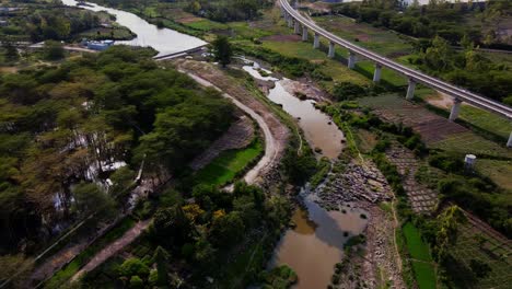 Suspended-Railway-Bridge-Near-Calm-River-Surrounded-With-Green-Areas