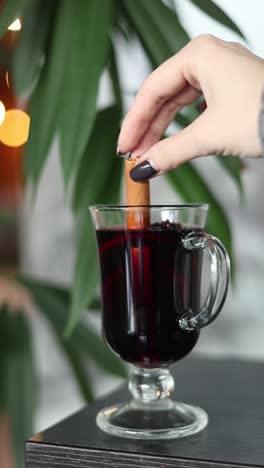 woman adding cinnamon stick to mulled wine