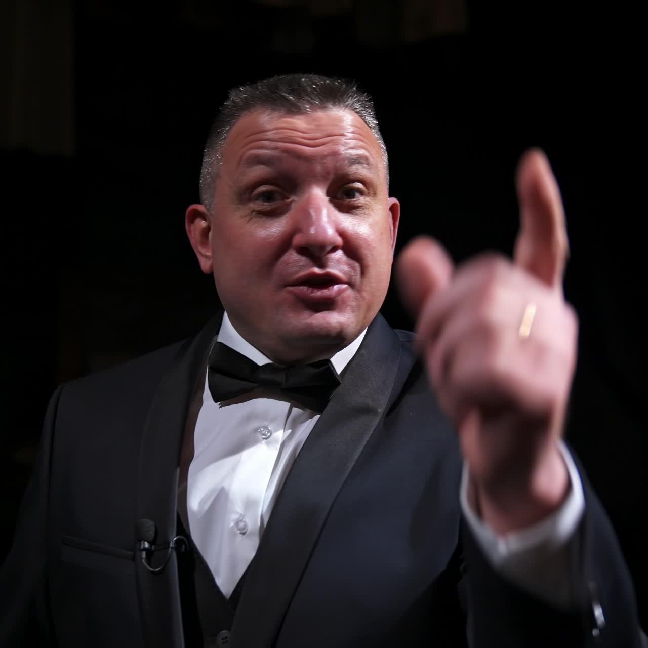 Actor in rich grey suit announces performance before auditorium. Theater curtains background. Dark background. Video from below