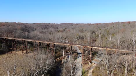 aerial shot pushing forward along a road towards the pope lick railroad trestle in louisville kentucky, with a forest in the background on a sunny day