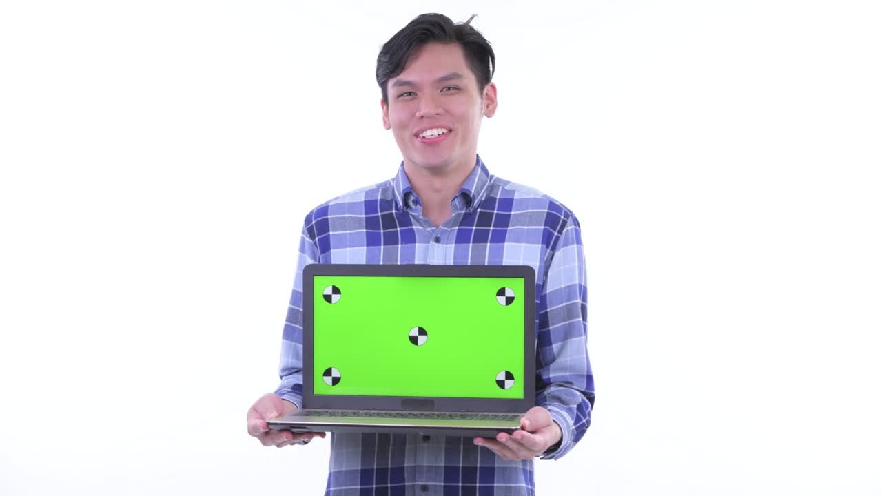 젊은 잘생긴 아시아 남자의 초상화 미소 짓고 하 배경에 고립 된 녹색 화면으로 노트북을 보여줍니다.