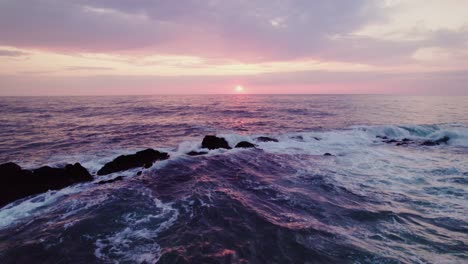 sunset over the ocean with rocks and waves