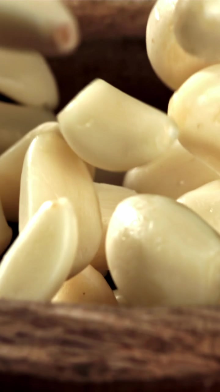 Spicchi d'aglio freschi e pelati che cadono in una ciotola di legno al rallentatore