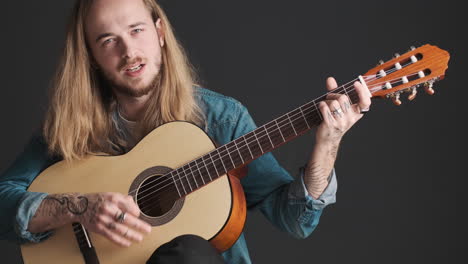 Caucasian-young-man-playing-guitar-and-singing-on-camera.