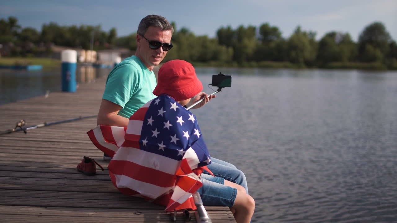 Father and Son Taking a Selfie by the Lake with American Flag