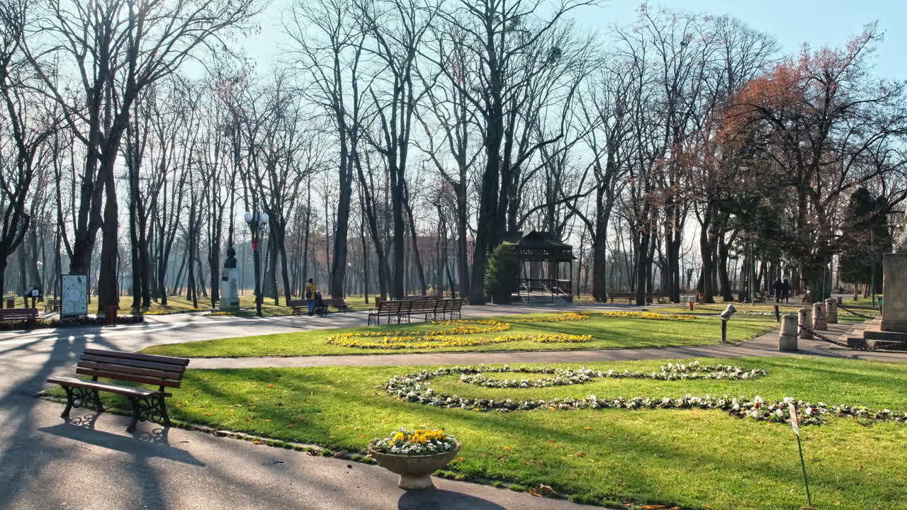 View of Copou Park in Iasi, Romania. Lions Obelisk, alleys, bare trees, green grass and flower beds, people
