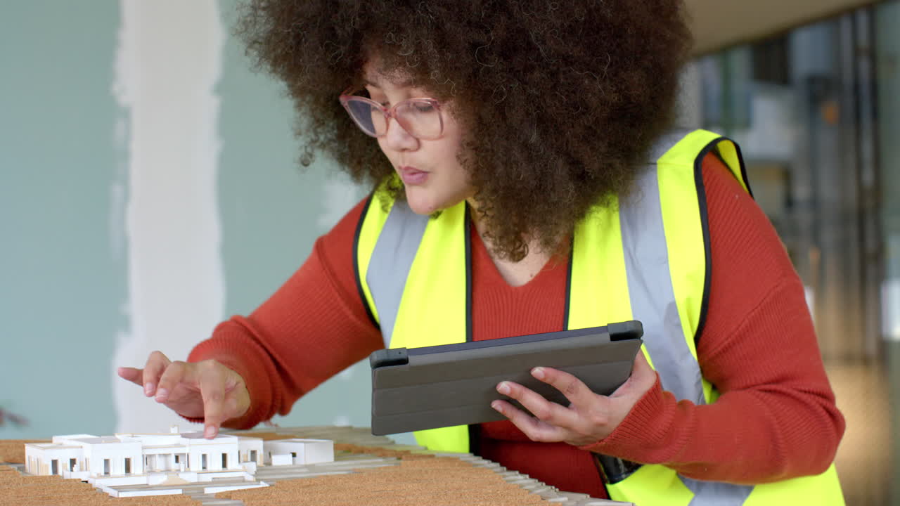 Casual biracial female architect with tablet looking at 3d model in office, slow motion, copy space