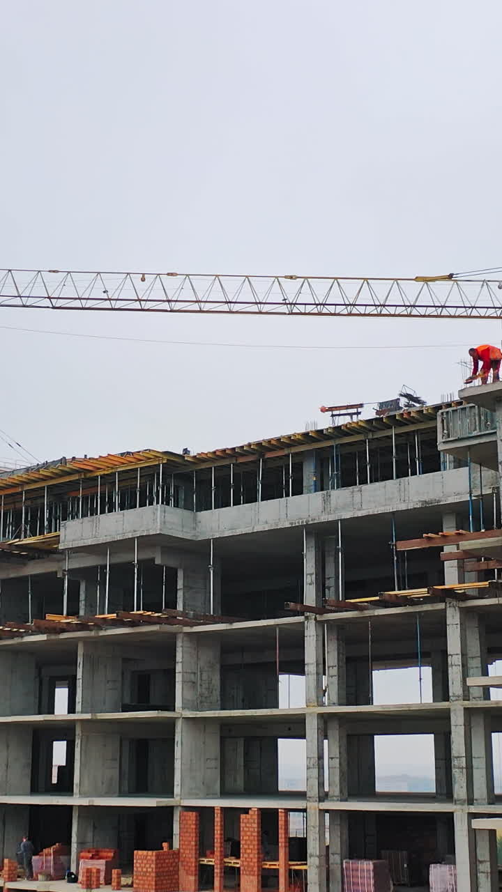Drone view on a new construction site. Working process of construction the modern building on the background of two big cranes in the city. Vertical video