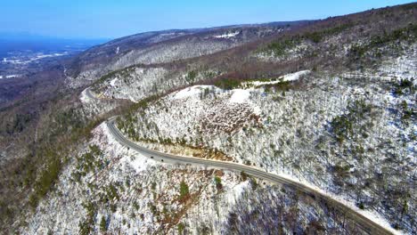 Aerial-drone-video-footage-of-a-snowy,-blue-sky-mountain-valley-road-highway-through-the-mountains-in-the-Appalachians-on-the-Shawangunk-ridge,-in-new-York-state