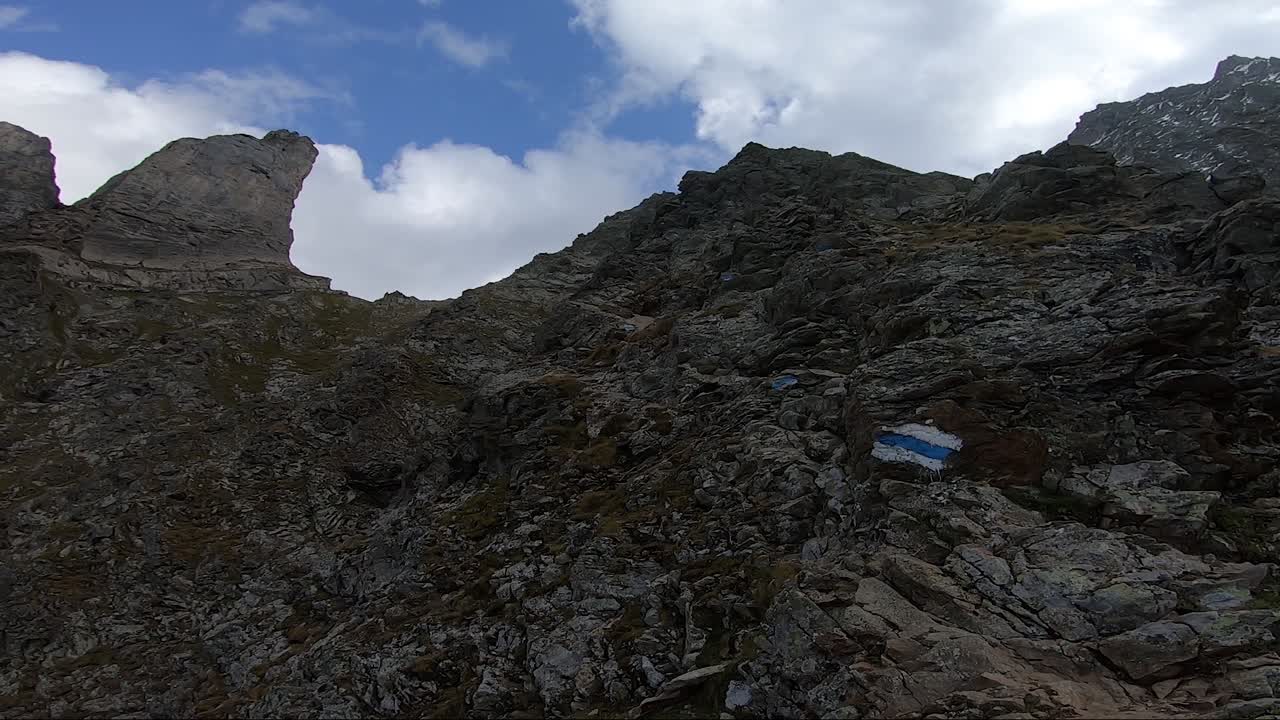 toma pov de un brazo tatuado y una mano que señala el camino hacia la cima de la montaña en suiza en el verano con cielo azul y nubes blancas hinchadas
