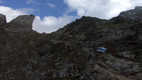 POV-shot-of-a-tattooed-arm-and-hand-pointing-the-way-up-the-trail-to-the-top-of-the-mountain-in-Switzerland-in-the-summer-with-blue-sky-and-white-puffy-clouds