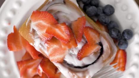 Homemade-Frosted-Cinnamon-Bun-with-Blueberries-and-Strawberries-on-Plate