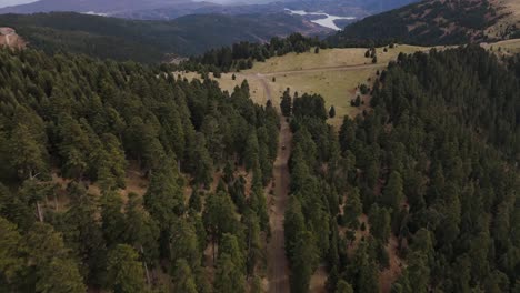 suv drives along dirt road between tall forested mountain pass up above agrafa, drone tracking