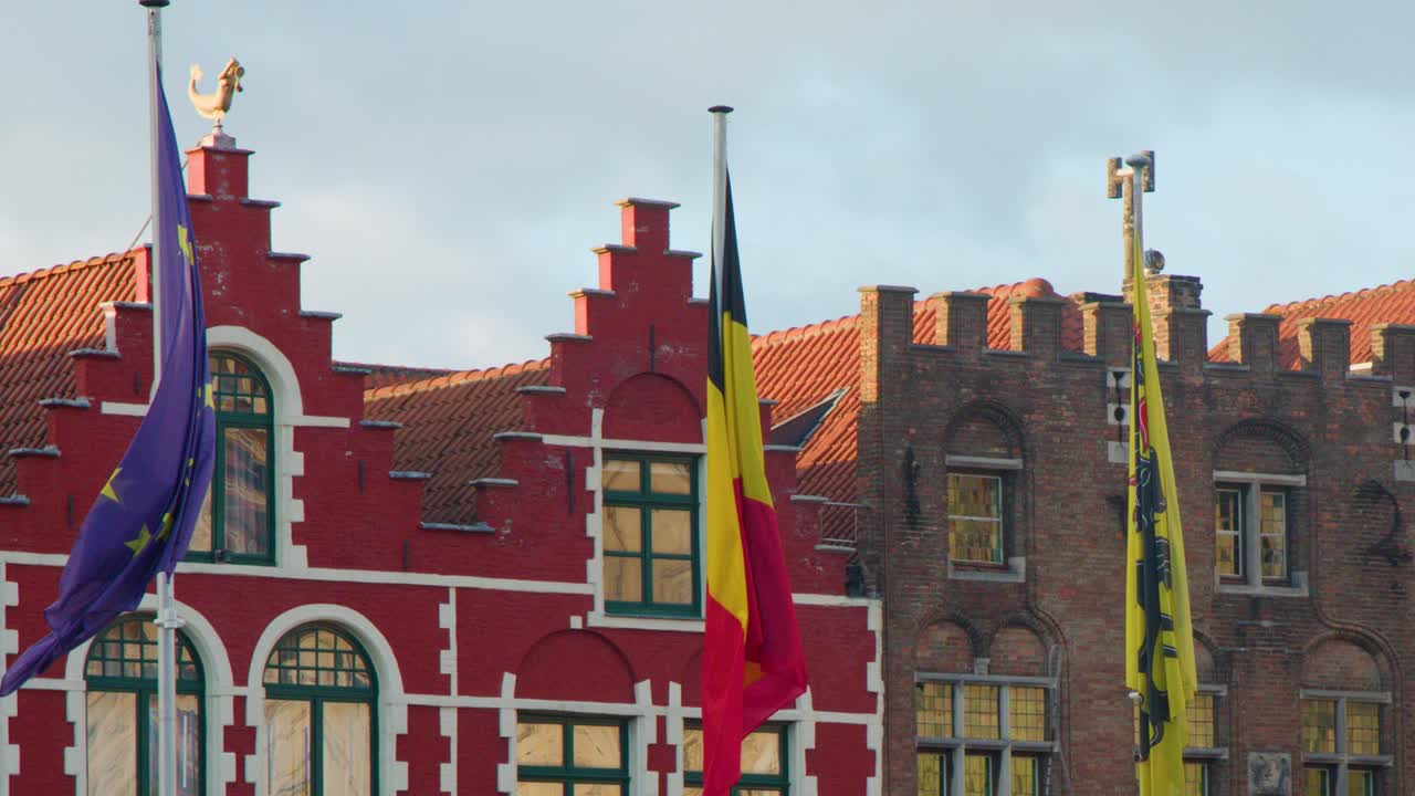 Colorful flags wave in evening light above historic gabled rooftops in Bruges city center