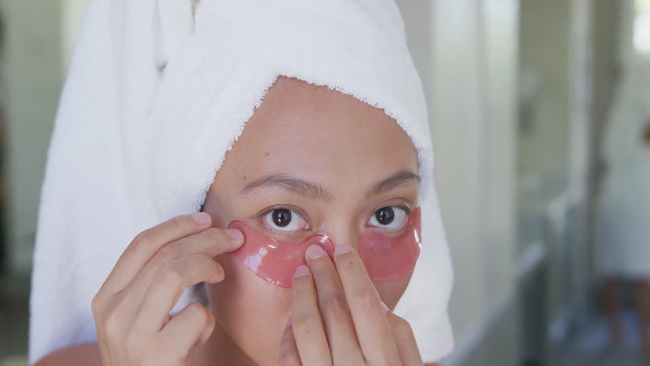 Happy asian woman applying eye patches in bathroom, in slow motion