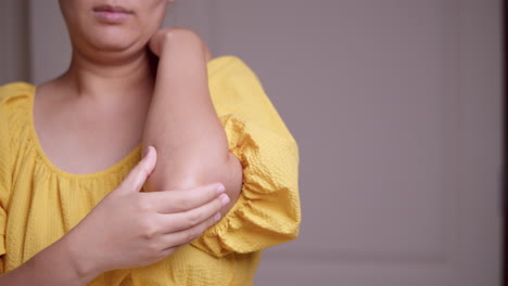 woman in yellow shirt is pinching and massaging her elbow to relieve the pain and inflammation of her arms and joints