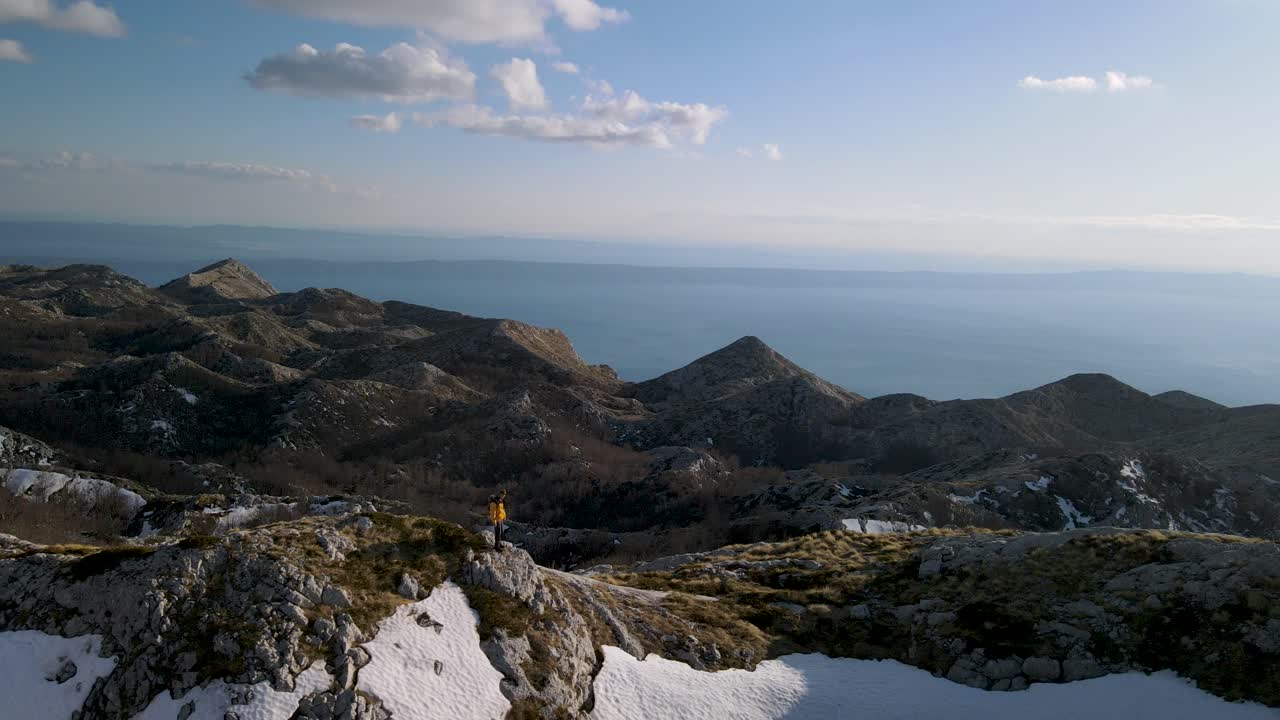 hombre haciendo senderismo en la cima de las montañas blancas nevadas contra el azul del mar adriático, sveti jure, biokovo, croacia