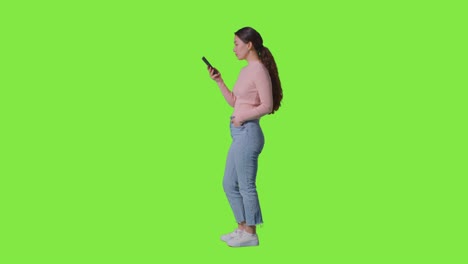 fotografía de estudio de perfil completo de una mujer usando un teléfono móvil contra una pantalla verde