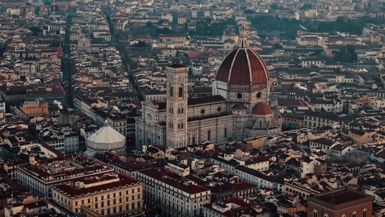 Aerial ascending retreat over Florence Duomo at sunrise, golden light illuminating the historic rooftops, strong contrasting dark roofs and grey buildings