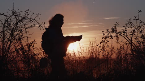 a lone tourist standing on the horizon with a map during sunset