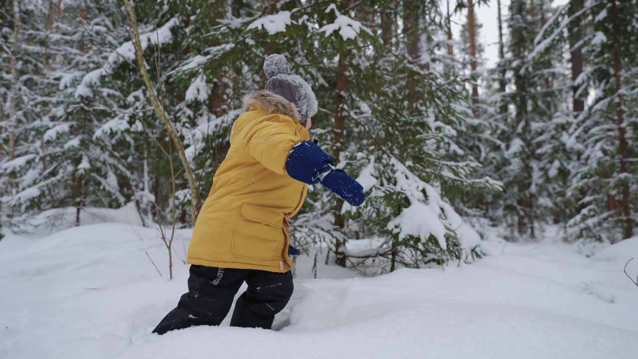 un niño con una chaqueta amarilla camina a través de la nieve profunda estudiando los paseos invernales del bosque invernal y a través del bosque nevado en cámara lenta. el concepto de un entorno libre para los niños