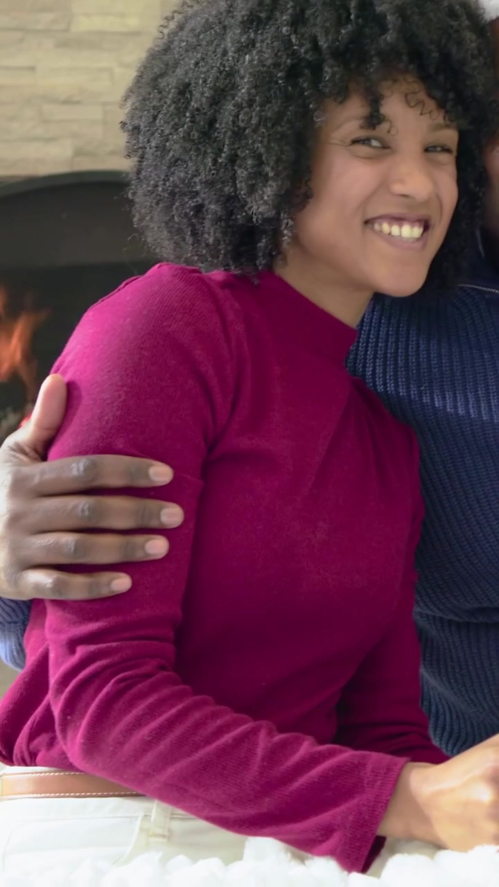 Video verticale: Notando il telefono, una donna con top magenta che si china a controllare il telefono e sorride vicino al caminetto.