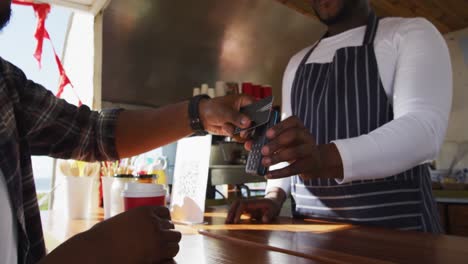 midsection of african american man paying male owner for coffee by credit card at food truck