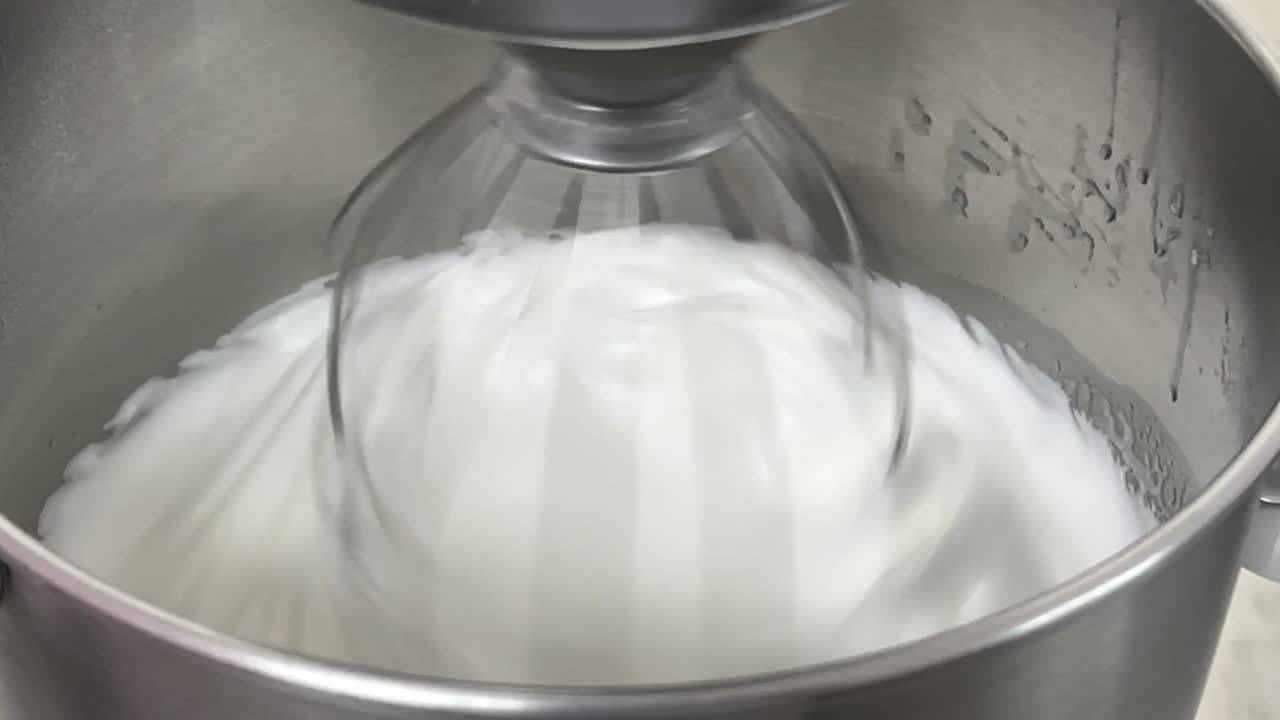 deliciosa pastelería en progreso, cocina comercial en primer plano toma de una batidora eléctrica mezclando clara de huevo y azúcar hasta que esté brillante y rígida, preparando crema de mantequilla de merengue
