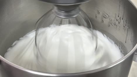 deliciosa pastelería en progreso, cocina comercial en primer plano toma de una batidora eléctrica mezclando clara de huevo y azúcar hasta que esté brillante y rígida, preparando crema de mantequilla de merengue