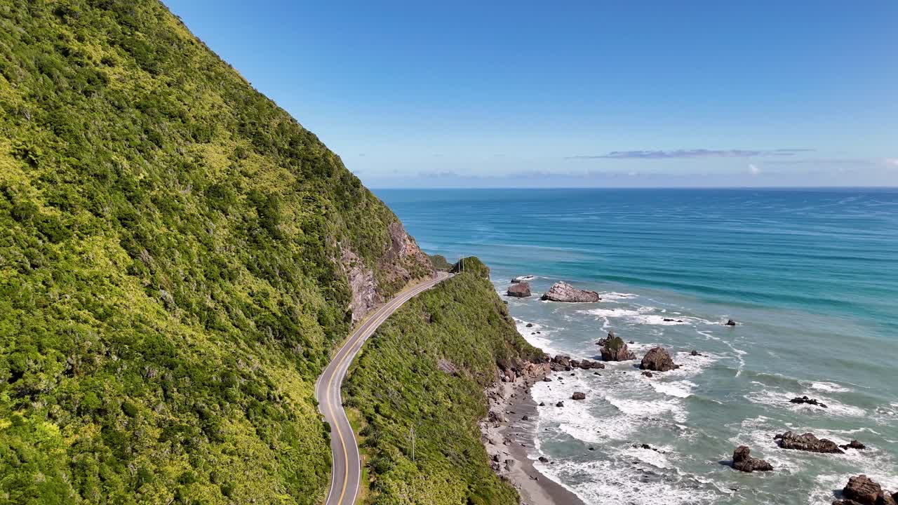 A 4K drone flies along a coastal road in New Zealand’s South Island. The drone captures cliffs, ocean waves, and mountains for a stunning aerial view of the dramatic coastline