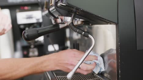 Hands-of-caucasian-male-barista-cleaning-coffee-machine-with-cloth-in-cafe