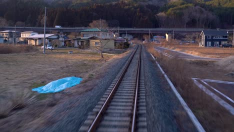 view from back of train riding through japanese countryside with few houses