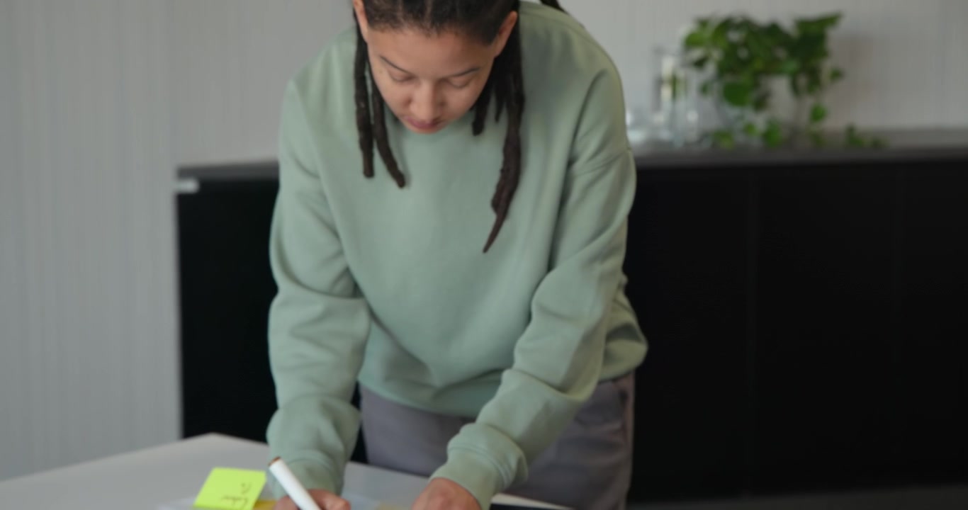 African nonbinary person writing Logo on yellow note arranging swatches in meeting room planning